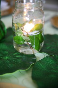 a jar filled with water sitting on top of a green leafy table cloth next to a vase