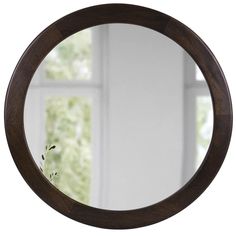 a round mirror hanging on the wall in front of a white wall with a window behind it