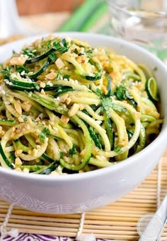 a white bowl filled with zucchini noodles and sauce on top of a bamboo mat