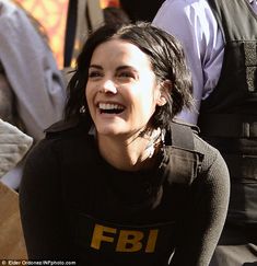 a smiling woman sitting on the ground with other people behind her