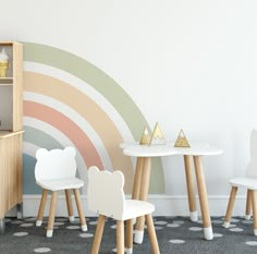 three children's chairs and table in front of a wall with a rainbow painted on it