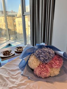 a bouquet of flowers sitting on top of a bed next to two plates of food