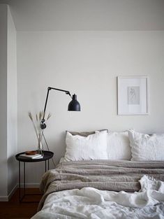 a bed with white linens and pillows in a bedroom next to a black lamp