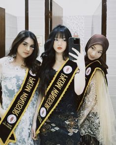 three beautiful young women standing next to each other in front of a mirror holding up their cell phones