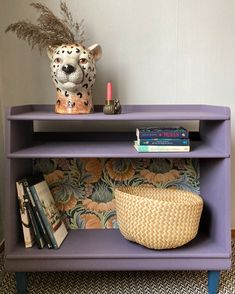 a purple shelf with books and a basket on it, next to a leopard head