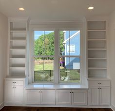 an empty room with built - in bookshelves and windows overlooking the yard outside