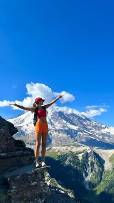 a woman standing on top of a mountain with her arms outstretched