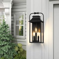 three candles are lit on the side of a wall light in front of a house