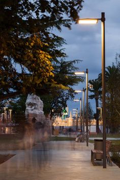 blurry image of people walking down a sidewalk at night with street lights and trees in the background