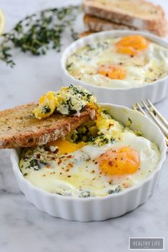 two bowls filled with eggs and toast on top of a white counter next to slices of bread