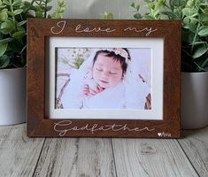 a small wooden frame with a baby's photo in it and some potted plants