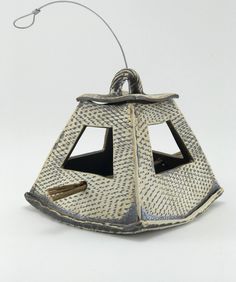 a small metal lantern on a white surface with a wire attached to the top and bottom