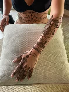 a woman with henna tattoos on her arm and hand is sitting on a pillow