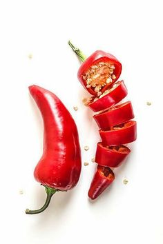 two red peppers cut in half on a white surface with seeds scattered around the whole pepper