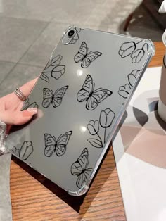 a woman's hand is holding an ipad case with butterflies on it and a coffee cup in the background