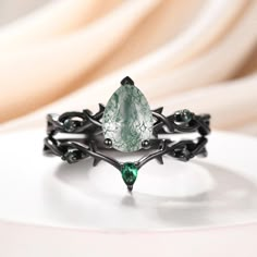 a ring with a green stone surrounded by black metal spikes and leaves, on top of a white surface