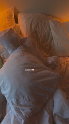 an unmade bed with white sheets, pillows and a yellow light in the corner