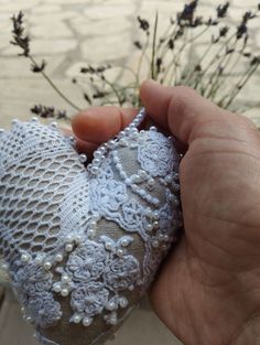 a hand holding a piece of lace with flowers in the background