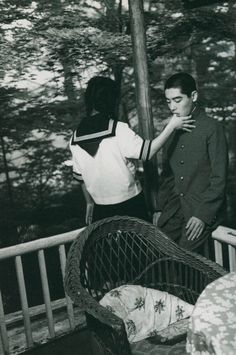 an old black and white photo of two people standing on a porch next to a baby crib