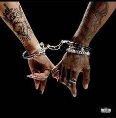 two hands holding each other with tattoos on their arms and wrist chains attached to them