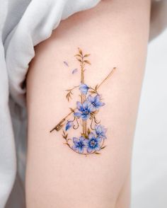 a tattoo with blue flowers on the side of a woman's thigh and an arrow