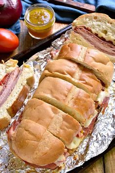 two sandwiches cut in half sitting on top of tin foil next to tomatoes and bread