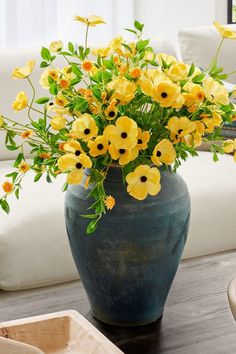 a blue vase filled with yellow flowers sitting on top of a table next to a white couch