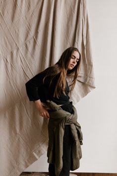 a woman standing on top of a wooden floor next to a white wall in front of a curtain