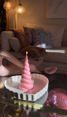 a pink candle sitting on top of a glass table next to a white couch in a living room