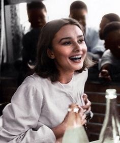 a smiling woman sitting at a table in front of bottles