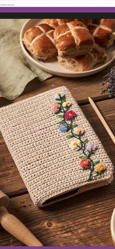 a crocheted book with flowers on it next to some bread and other items