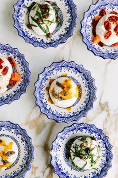 four blue and white plates filled with food on top of a marble countertop next to each other