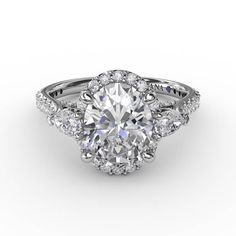 Pear-shape diamond accents elegantly wing out from the sides of this oval diamond halo engagement ring. It’s a glamorous style, with an intricately structured gallery, and diamond band, to enhance the display of light. Available in platinum, 18KT & 14KT gold. Center stone sold separately.  Style #S3280.