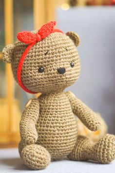 a small crocheted teddy bear with a red bow on its head sitting on a bed