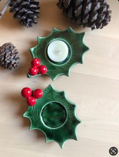 two holly berry candle holders on a table with pine cones and candlesticks next to them