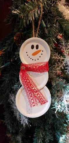 a paper plate snowman ornament hanging from a christmas tree with red ribbon