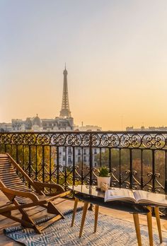 two wooden chairs sitting on top of a balcony overlooking the eiffel tower in paris