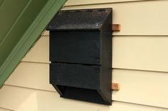 a black wooden box mounted to the side of a house next to a green door