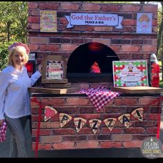 a woman standing in front of an outdoor pizza oven that is decorated with red and white checkered cloths