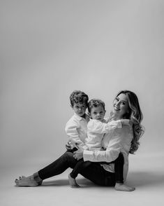 a woman sitting on the ground with two children in her lap and one child holding him