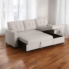 a white couch with a pull out bed underneath it on a hard wood floor next to a window