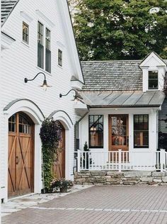 a white house with two brown doors and brick walkway leading up to the front door