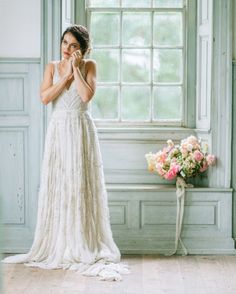 a woman standing in front of a window holding her hands to her face and wearing a wedding dress