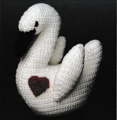 a crocheted white swan with a heart on it's chest sitting in front of a black background