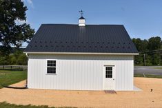 a white barn with a black roof and two windows on the top floor is shown