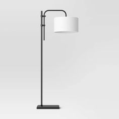 a floor lamp with a white shade on it's head and black metal frame