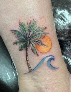 a small palm tree and wave tattoo on the foot with an orange sun in the background