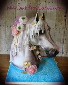 a white horse with flowers on it's head sitting on top of a table