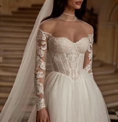 a woman wearing a wedding dress with long sleeves and a veil on her head is standing in front of stairs