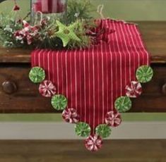 a red table cloth with green and white decorations sits on top of a wooden bench